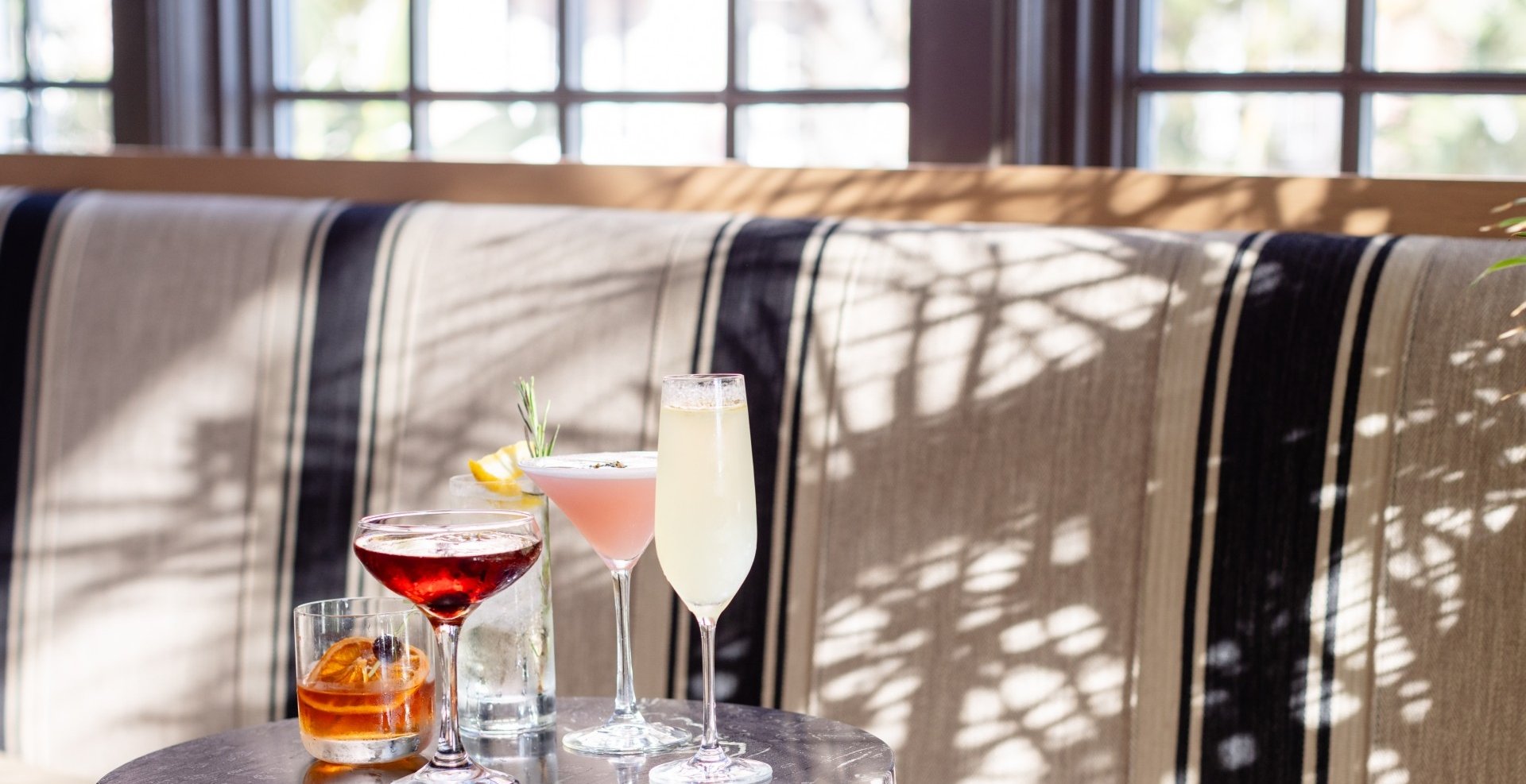 Three colorful cocktails on a table, illuminated by sunlight streaming through a window.