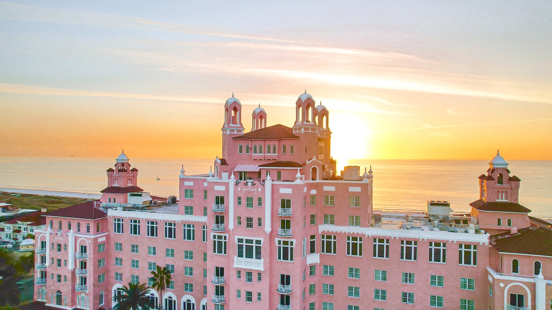 large pink hotel with the ocean in the background at sunset