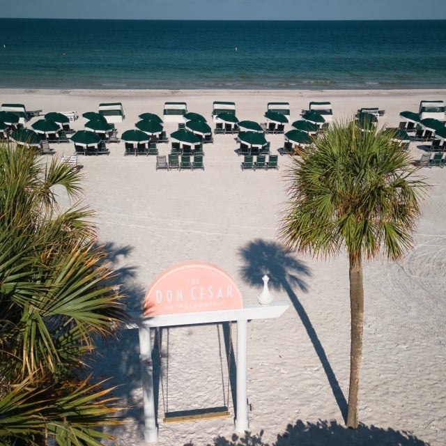 the beach with lounge chairs and a wooden swing