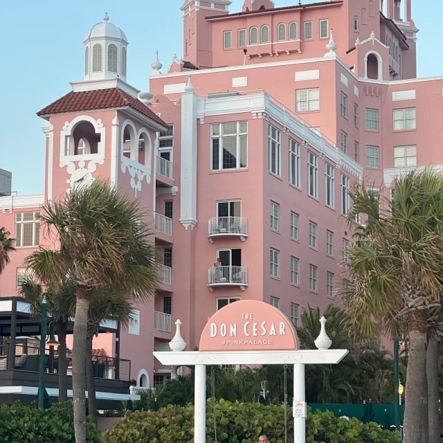 a couple swinging on the beach in front of a pink hotel