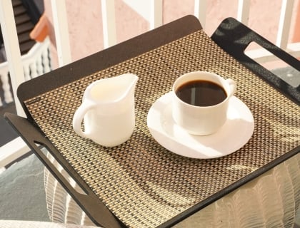 A tray with a steaming cup of coffee sits on a balcony, surrounded by a serene outdoor view.