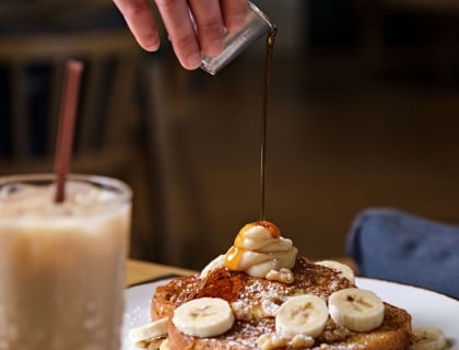 A person drizzles syrup over a plate of golden-brown French toast, enhancing its delicious appearance.