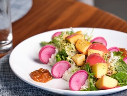 A colorful plate featuring fresh radishes, juicy peaches, and crisp cucumbers arranged artfully.