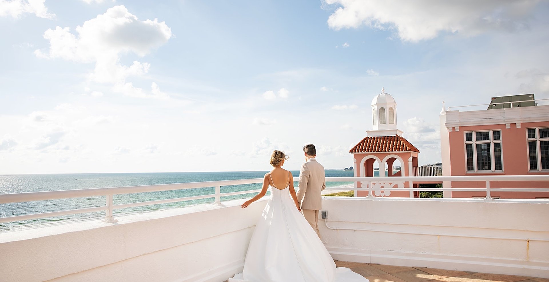 a bride and groom looking off of a balcony into the ocean