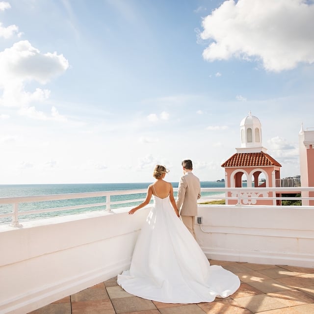 a bride and groom looking off of a balcony into the ocean