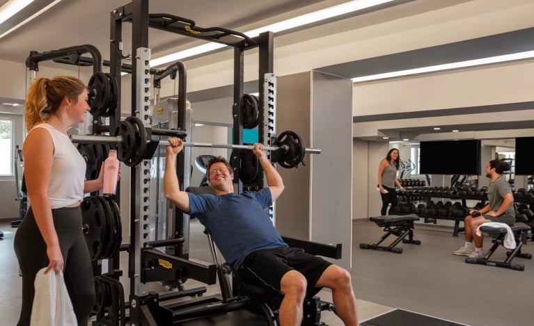 a woman spotting a man while he lifts a large weight