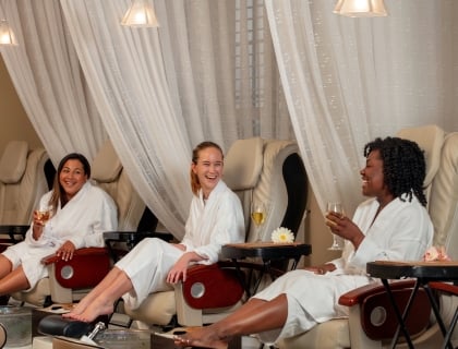 Three women drinking wine and laughing while getting pedicures