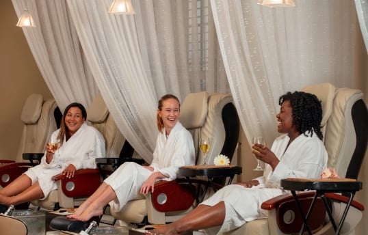 Three women drinking wine and laughing while getting pedicures