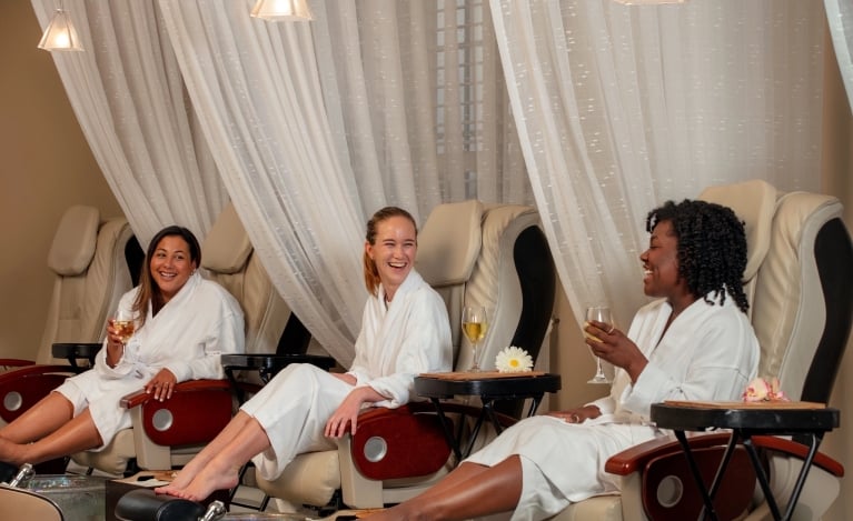 Three women drinking wine and laughing while getting pedicures