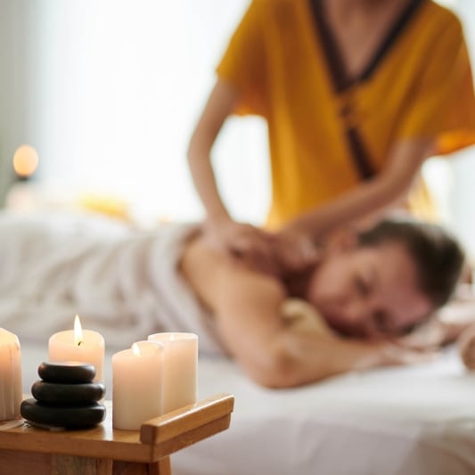 Burning candles in spa salon and woman getting back massage in background