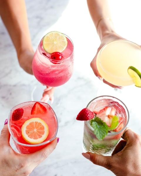 people holding colorful cocktails