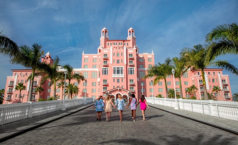 five women holding hands walking to the entrance of a hotel