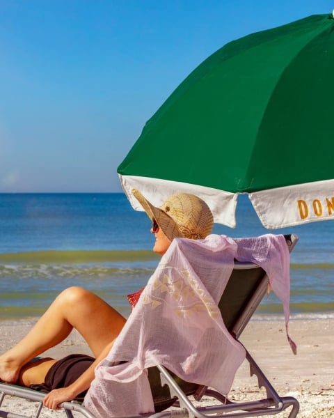 woman sitting on the beach under a green umbrella