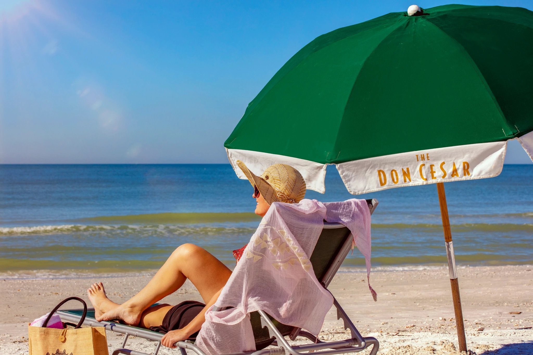 woman sitting on the beach under a green umbrella