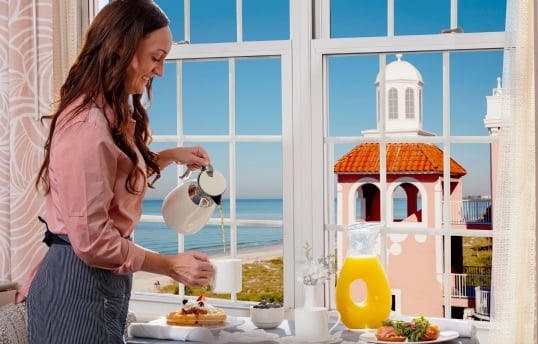 Woman pouring coffee near a window with a beautiful view of the beach