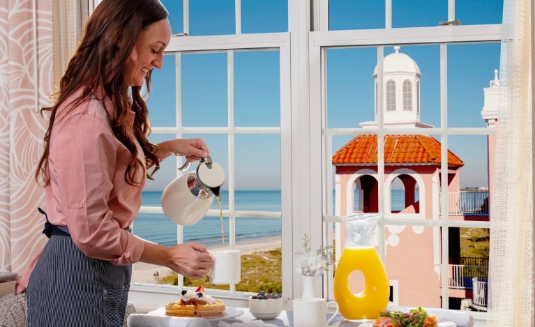 Woman pouring coffee near a window with a beautiful view of the beach