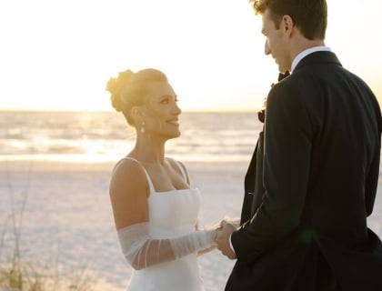 A bride and groom embrace on the beach, silhouetted against a vibrant sunset sky.