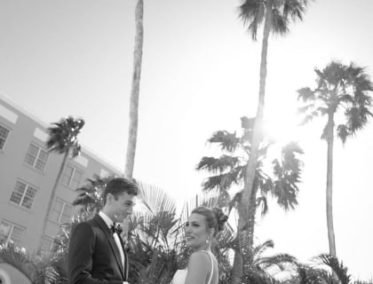 A bride and groom pose together in front of lush palm trees, radiating love and joy on their special day.