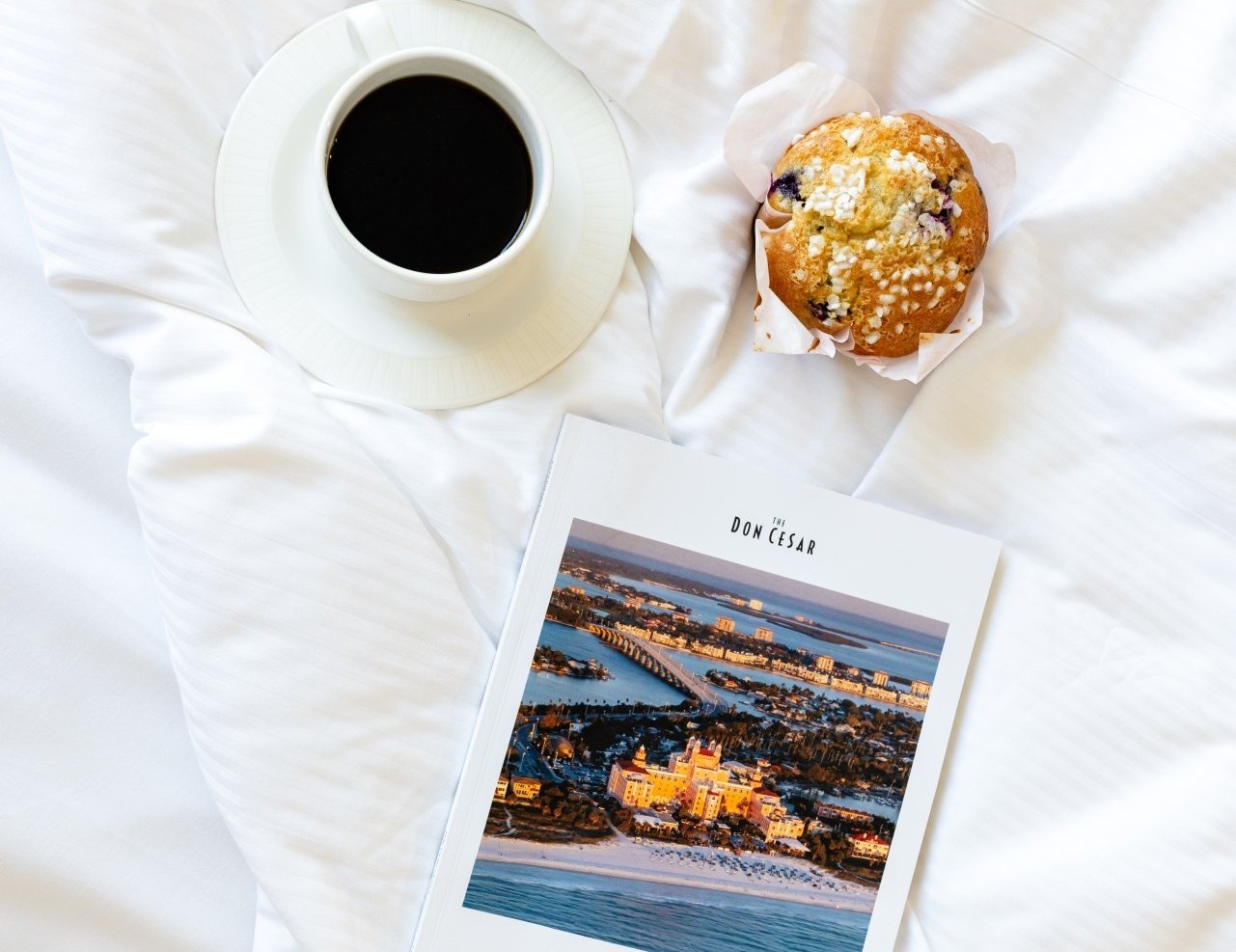 A cozy scene featuring a cup of coffee and a magazine resting on a neatly made bed.