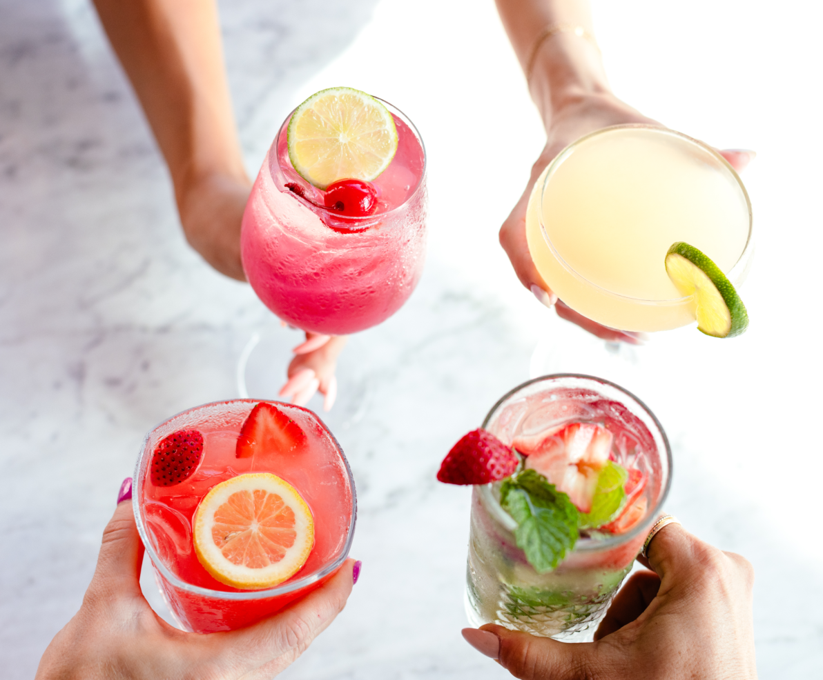 Four hands holding colorful cocktails