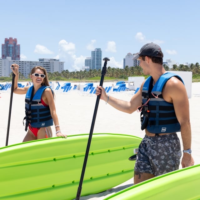 A man and a woman stand on the beach, each holding a paddle, ready for a day of fun on the water.