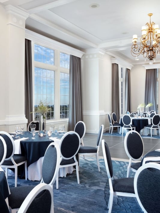 A spacious banquet room featuring blue tablecloths and white serviettes elegantly arranged on the tables.