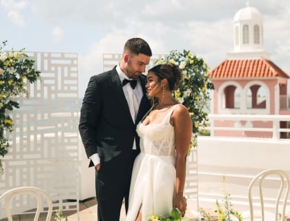 A bride and groom surrounded by flowers posing on a veranda