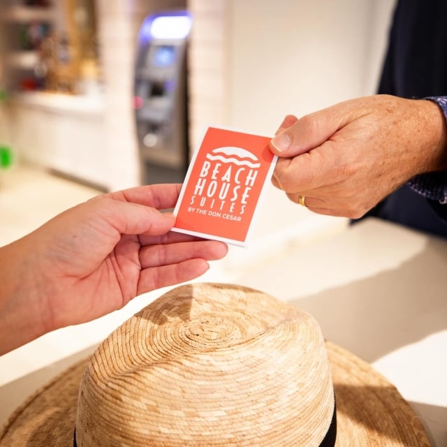 A front desk employee handing a Beach House Suites key card to a guest