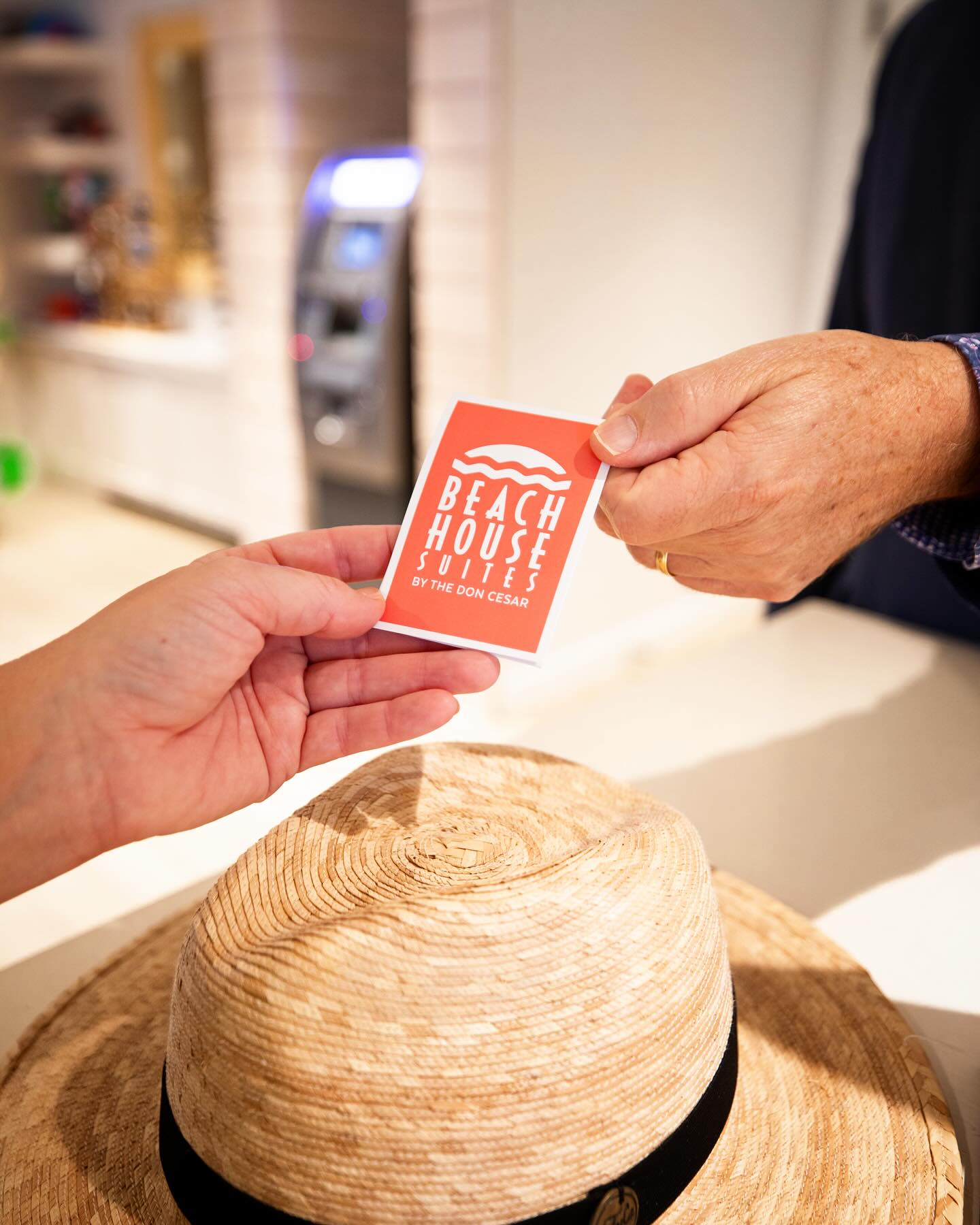 A front desk employee handing a Beach House Suites key card to a guest