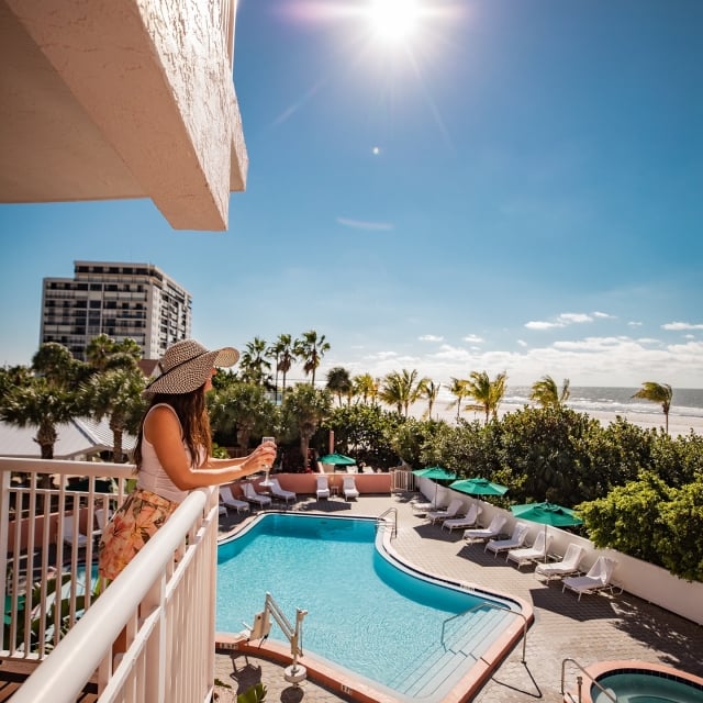 A woman on a balcony drinking champagne looking out over the pool