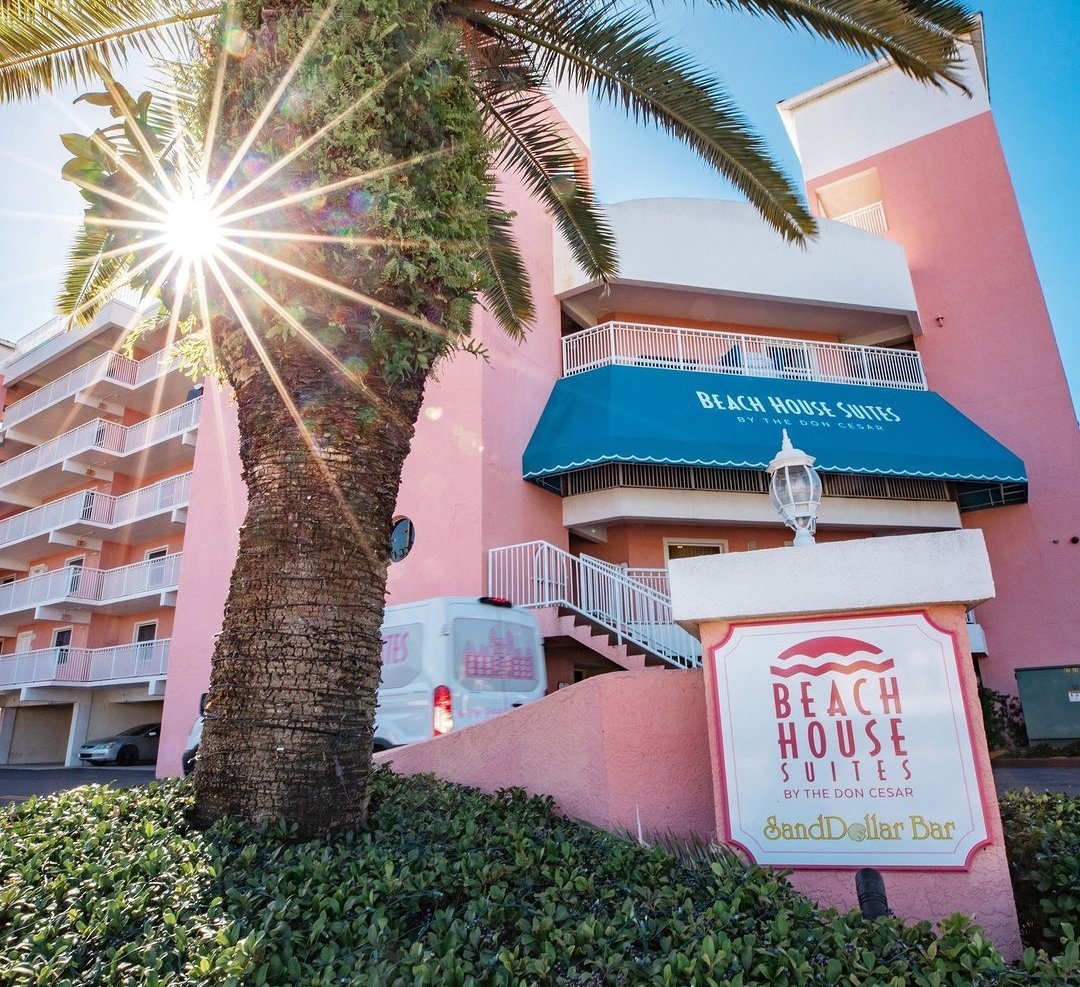 Entrance of the Beach House Suites with a palm tree in front and the sun shining bright