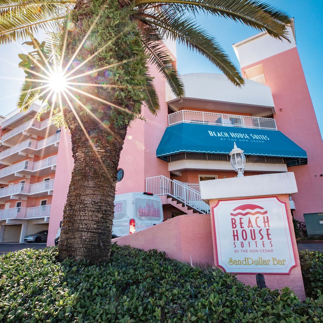 Entrance of the Beach House Suites with a palm tree in front and the sun shining bright